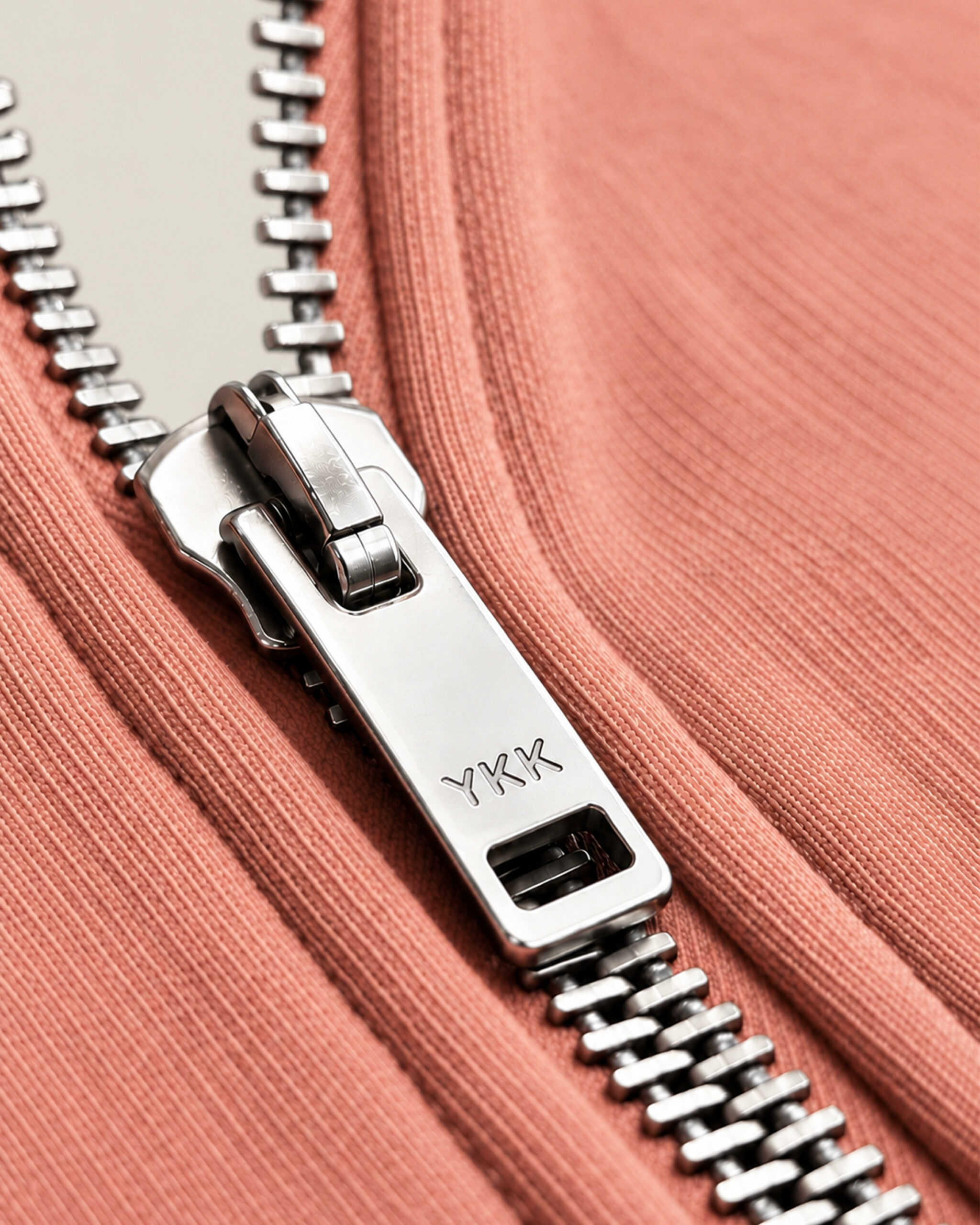 Geöffneter Metall-Reißverschluss mit YKK-Prägung auf dem Schieber an einem terrakottafarbenen Strickteil